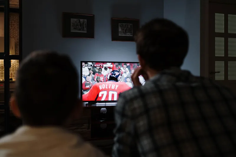 Two people watching a sports broadcast on a television at home in the evening