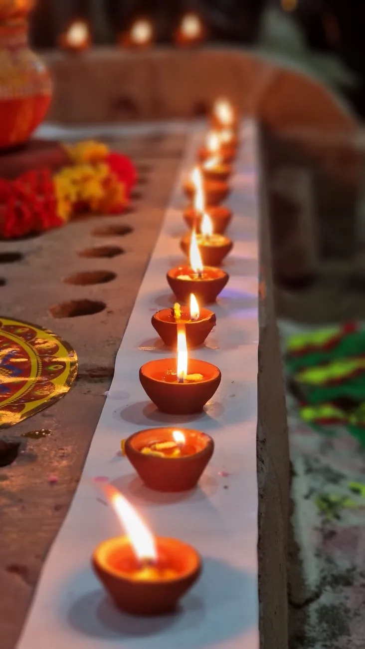 A row of lit clay diyas beside marigold flowers on a temple altar step