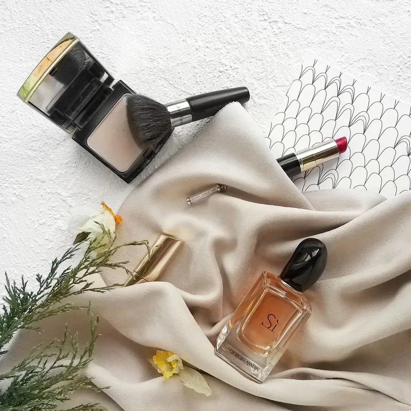 Makeup brush, powder and perfume arranged on a soft neutral cloth