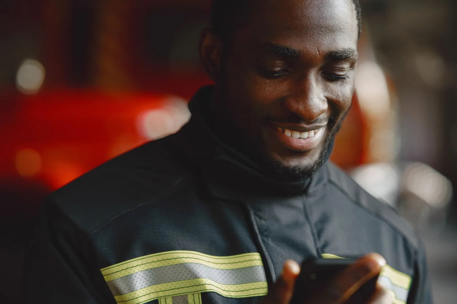 A frontline worker in a reflective-striped uniform smiling while reading a training lesson on his smartphone