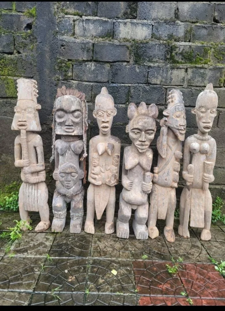 A row of hand-carved African ancestor figures standing against a stone wall