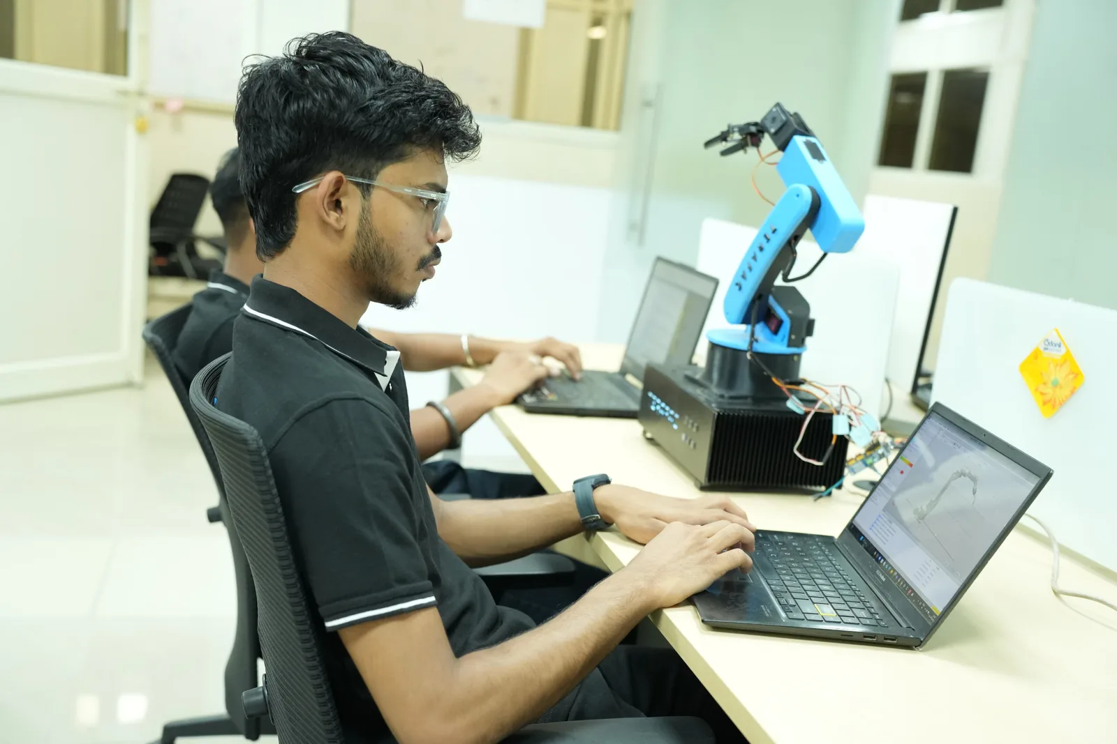 A Terafac engineer at a workstation programming a small cobot arm with CAD on screen